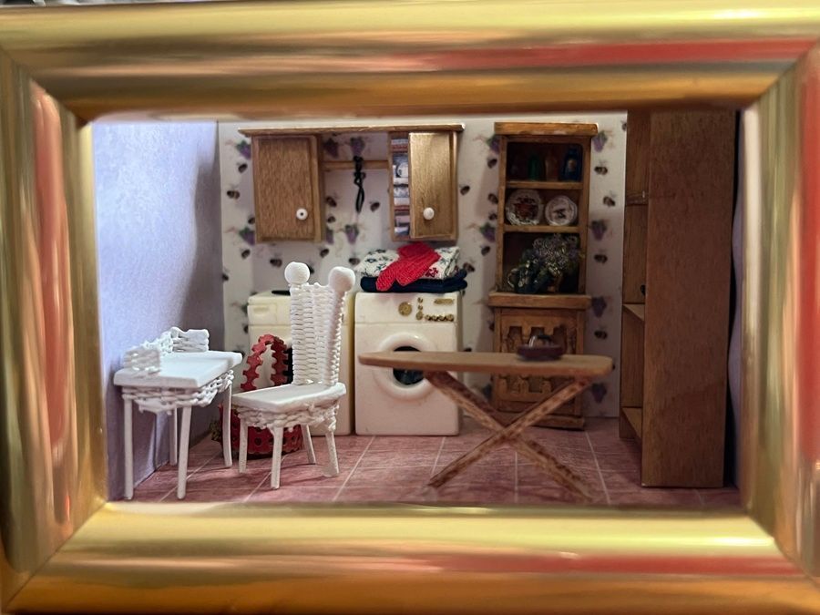 Miniature vintage kitchen and dining room scene in a gold frame, with table, chairs, cabinets, and dishes