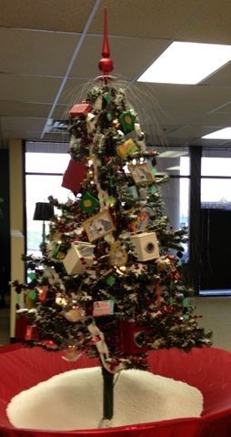 Decorated Christmas tree with ornaments and cards in an office lobby, wrapped in red and white fabric