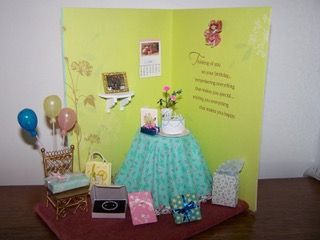 Decorated party display with green backdrop, gift table, balloons, flowers, and small chair in a room