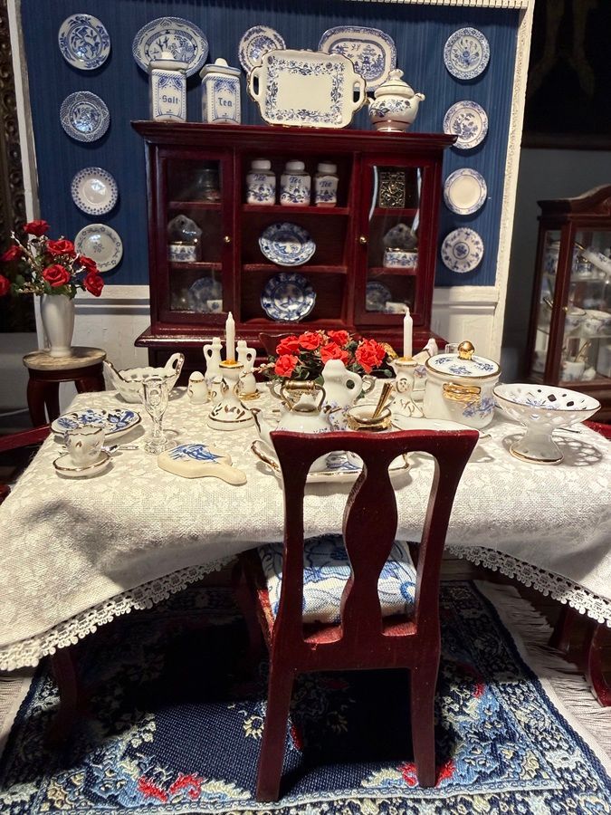Traditional dining room with red hutch, blue-and-white plates, and a set table with teacups and red flowers.