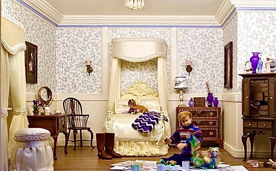 Victorian-style bedroom with ornate bed, vanity, chairs, and a child sitting on the floor among toys