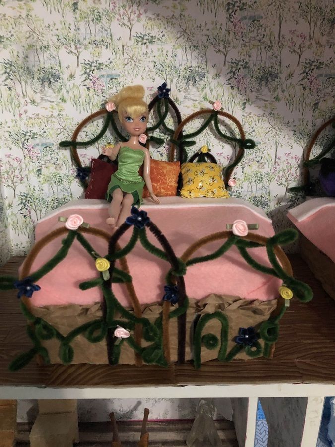 Decorated toy bed with a fairy doll, pink bedding, and floral wallpaper in the background