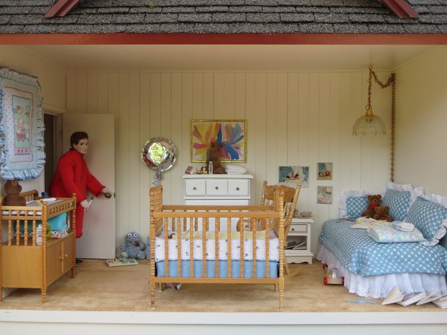 Colorful dollhouse bedroom with crib, bed, dresser, and a person standing by the door