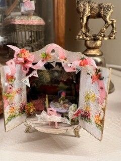 Pink paper dollhouse display with floral decorations and open doors on a table
