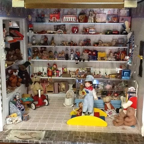 Cluttered toy room with shelves of stuffed animals, dolls, and miniature furniture, plus a doll in front.