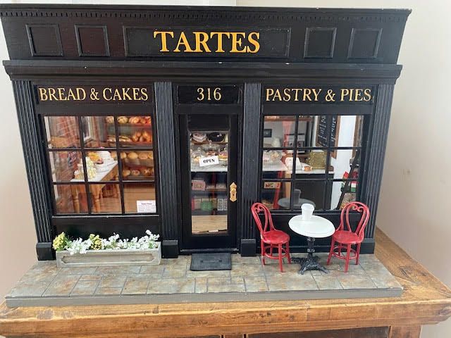 Miniature bakery storefront labeled “TARTES” with bread, cakes, pastries, and a small outdoor table and chairs