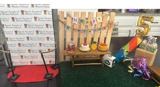 Birthday display with cake, balloons, gift table, and large gold number 5 on a green carpet
