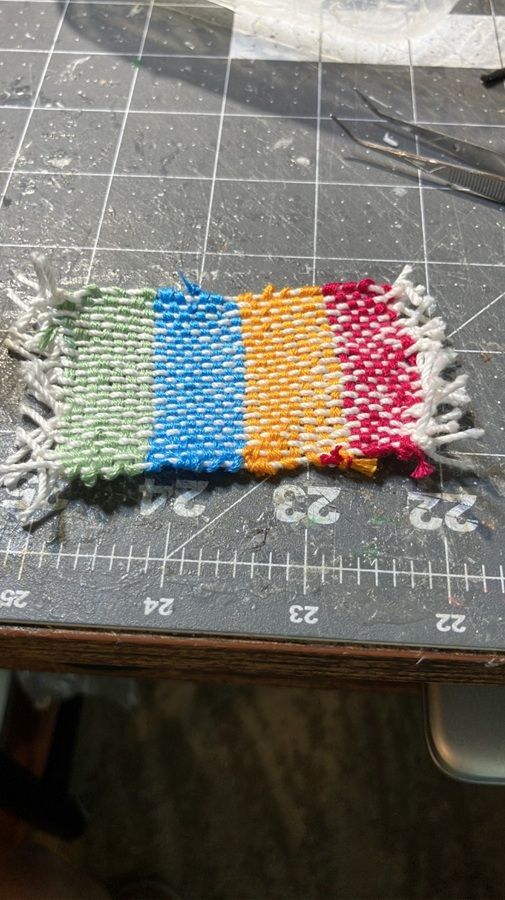 Small multicolored woven fabric swatch with green, blue, orange, red and white sections on a cutting mat