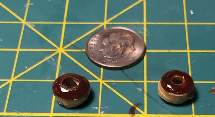 Two small brown beads beside a coin on a green cutting mat with yellow grid lines