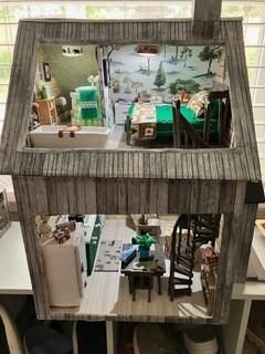 Two-story dollhouse interior with rustic walls, miniature furniture, and green-and-white rooms.