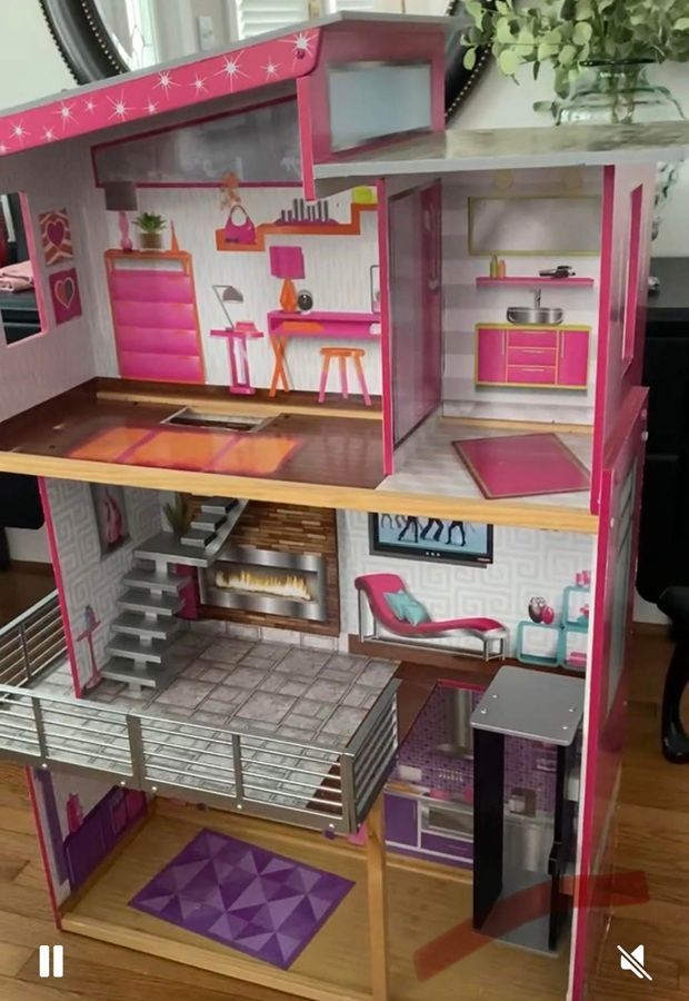 Three-story pink and gray dollhouse with furnished rooms and a staircase