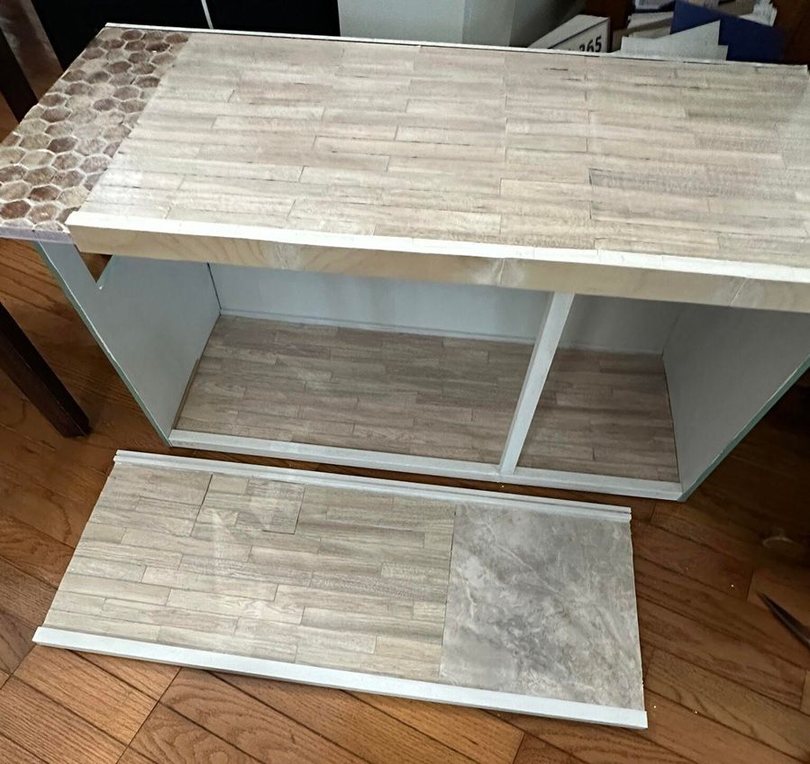 White cabinet with wood-grain top and sliding bottom panel removed, showing interior shelves on a hardwood floor.