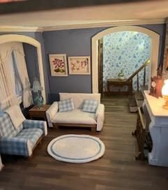 Miniature dollhouse living room with blue plaid chairs, white sofa, rug, and staircase opening