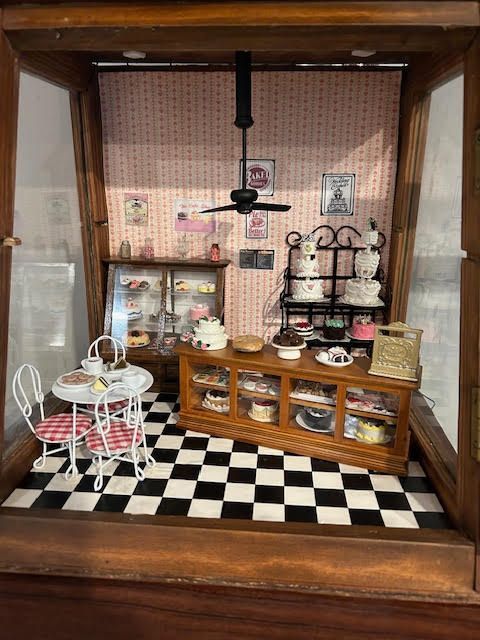 Miniature vintage-style kitchen dollhouse with black-and-white floor, wooden cabinets, and tiny tea set
