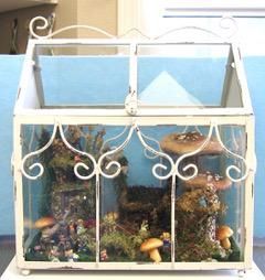 Decorative white terrarium with plants and mushrooms inside, framed by ornate scrollwork accents