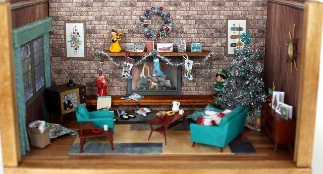 Miniature cozy living room with Christmas tree, fireplace, teal chairs, and festive holiday decor.