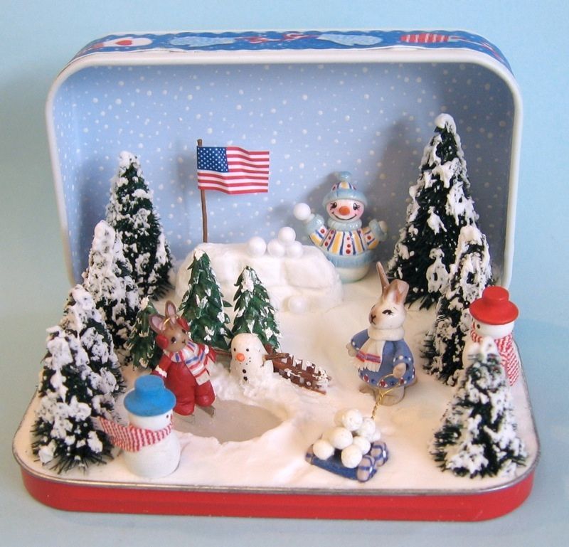 Snowy holiday display in a tin, with miniature trees, rabbits, a snowman, and a small American flag