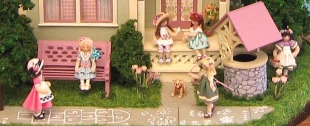 Miniature village scene with dolls at a pink cottage, stone well, and garden path
