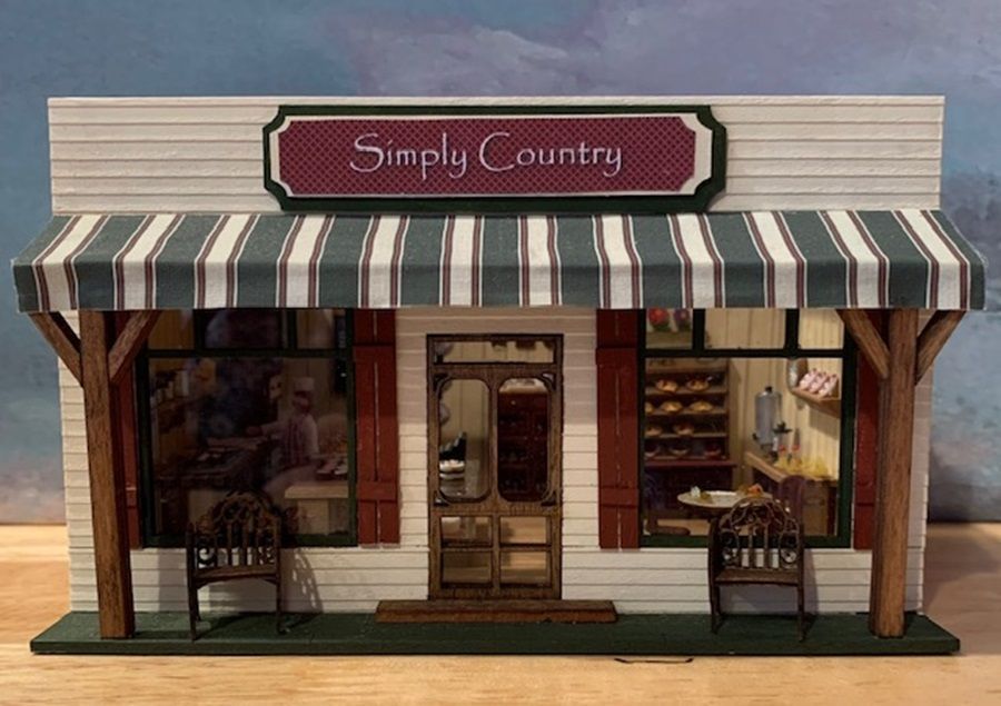 Miniature storefront labeled “Simply Country” with striped awning and rustic porch display