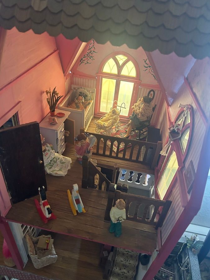 Miniature dollhouse interior with wooden balcony, arched window, and tiny figures in a warmly lit room