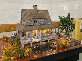 Miniature house model with porch, lit windows, and landscaped yard on a display table