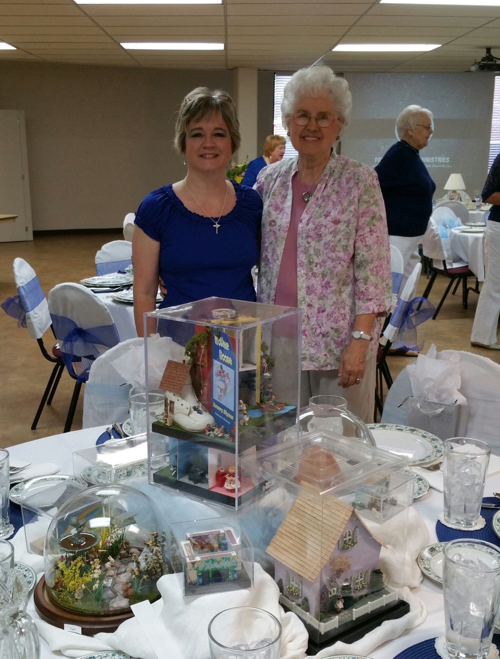 Two women standing at a decorated banquet table in a community hall