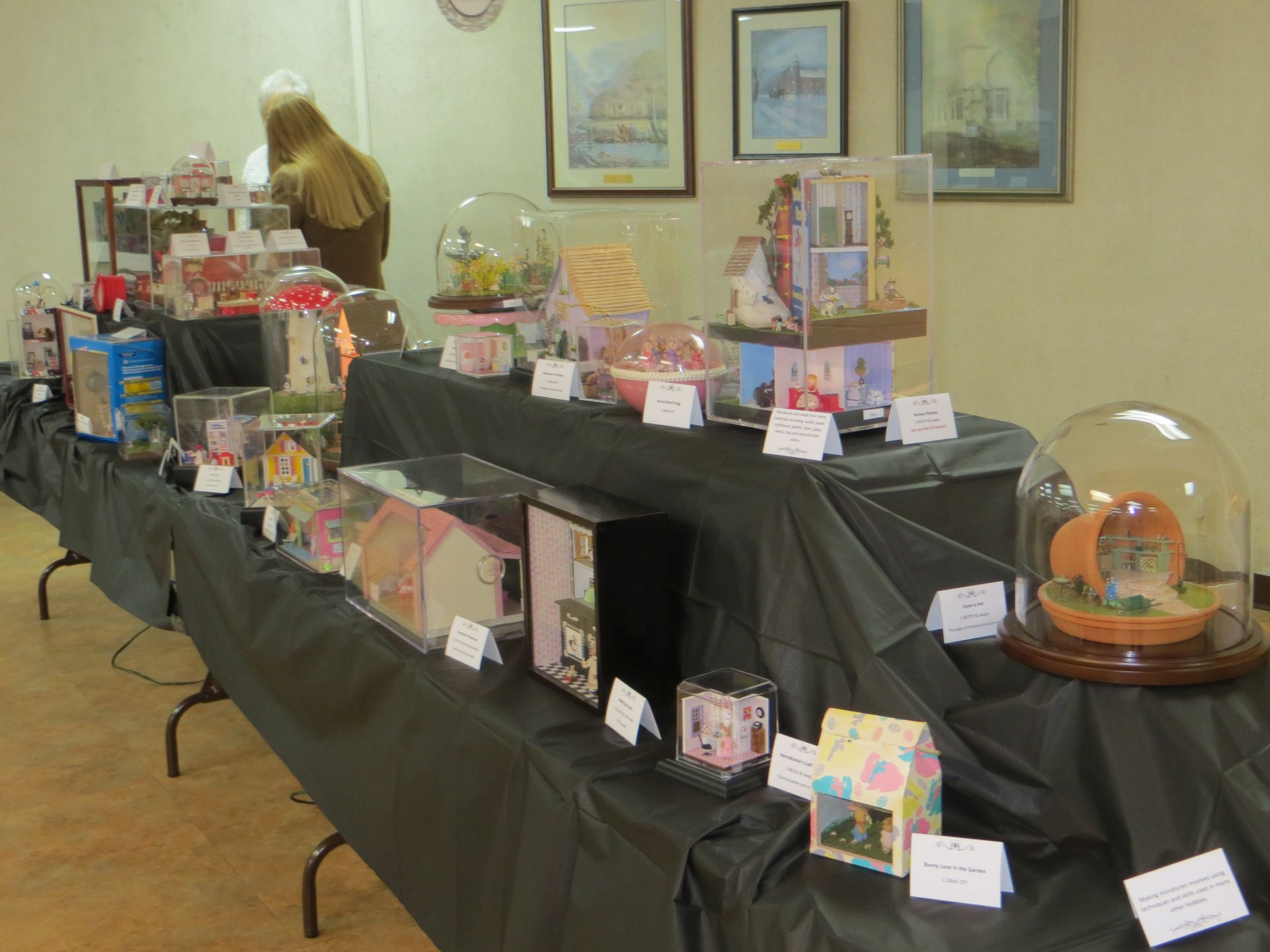 Table display of handmade crafts and gift baskets on black tablecloths at an indoor event