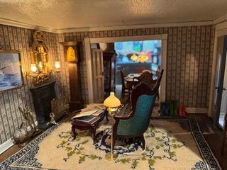 Elegant living room with patterned wallpaper, antique chairs, warm lamps, and a floral rug