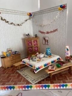 Birthday-decorated room with a low table, gifts, balloons, and colorful paper garlands in the corners