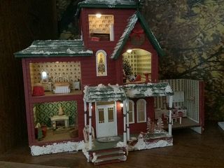 Red Victorian-style dollhouse with lit windows, white trim, and a front porch on a dark background