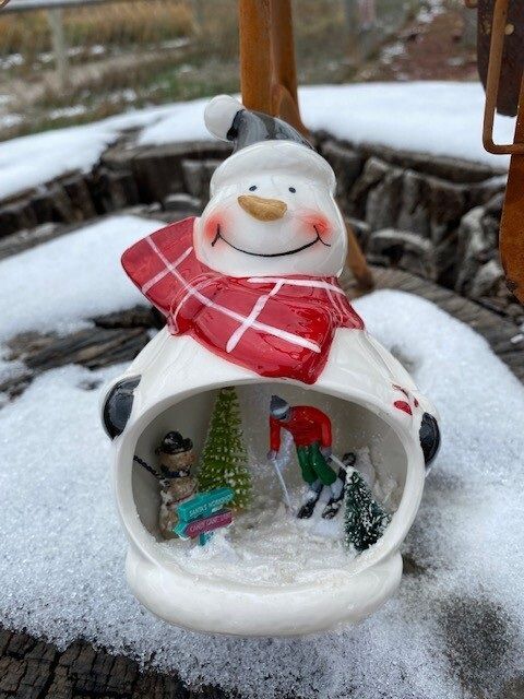 Snowman ornament with red scarf, hanging outdoors in the snow