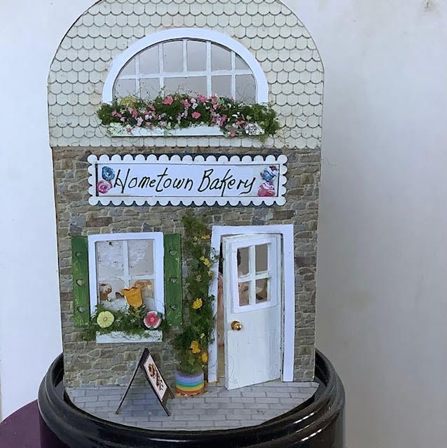 Miniature storefront labeled “Hometown Bakery” with white door, flower boxes, and scalloped roof detail