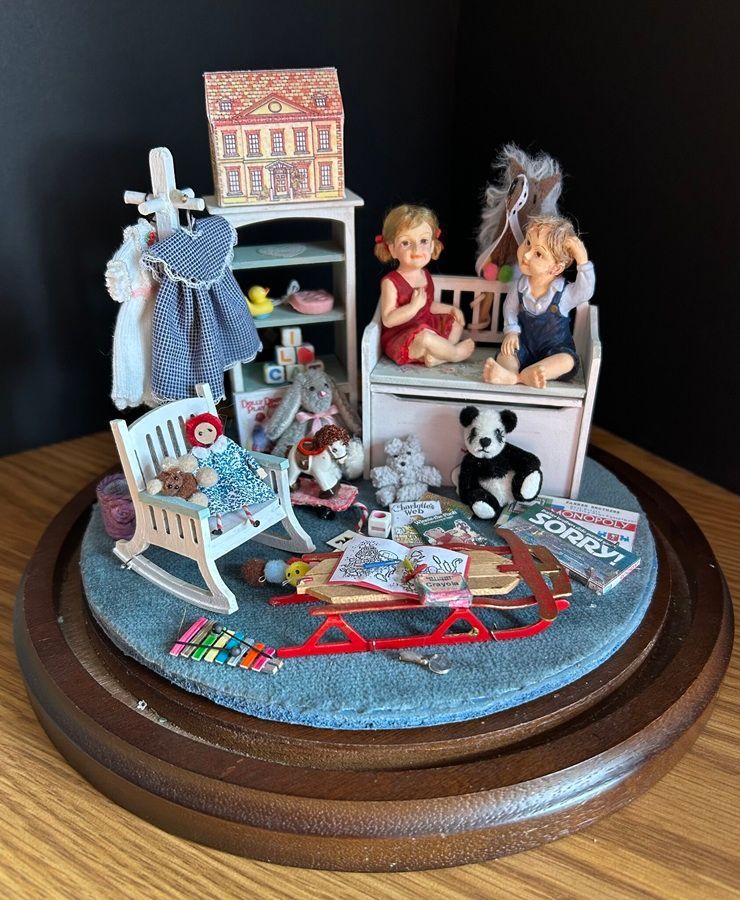 Miniature bedroom scene on a round base with two dolls, a panda, blue rug, and tiny furniture.