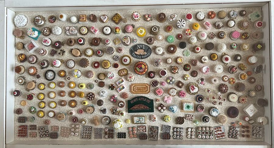 Wall display of dozens of colorful pins and badges arranged in rows on a beige background.