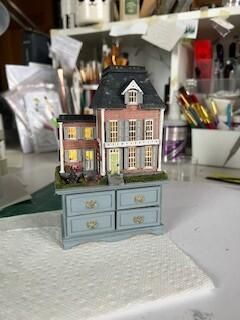 Miniature Victorian house model atop a light blue drawer cabinet on a craft table.