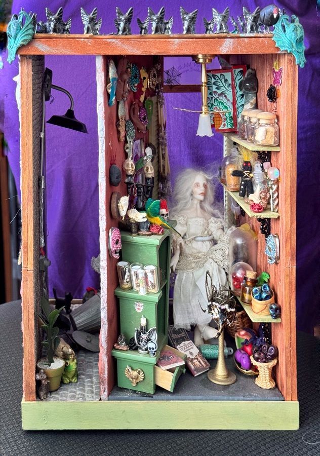 Miniature dollhouse room with purple walls, a seated ghostly figure, shelves of tiny objects, and hanging clothes