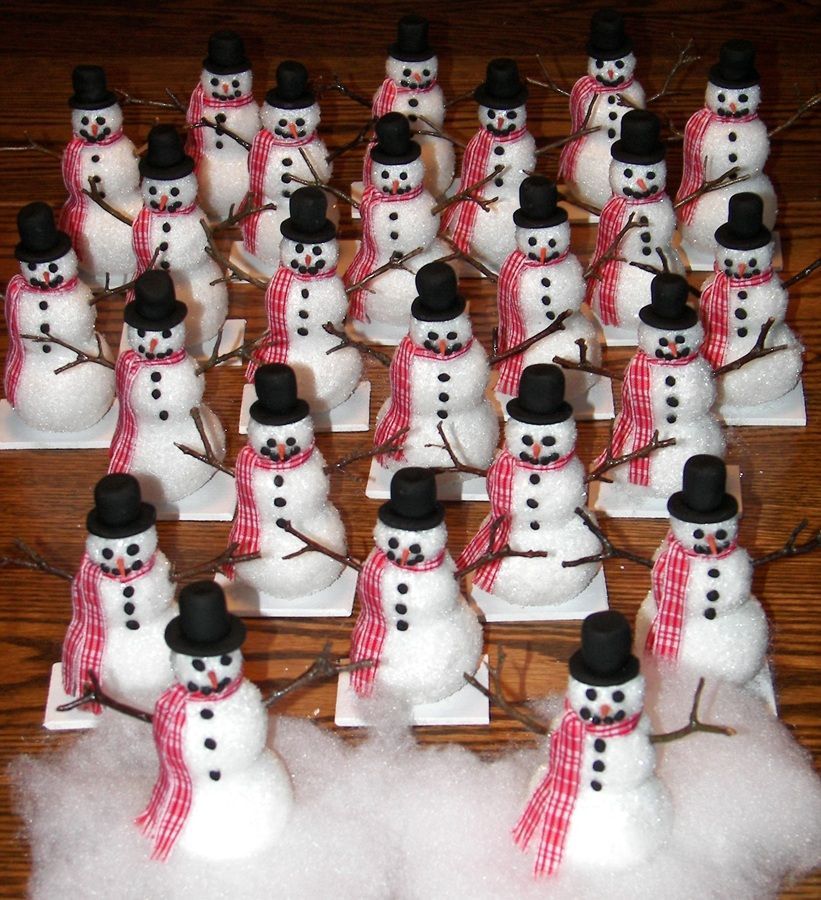 Rows of small snowman figurines with black hats and red scarves arranged on fluffy white snow.