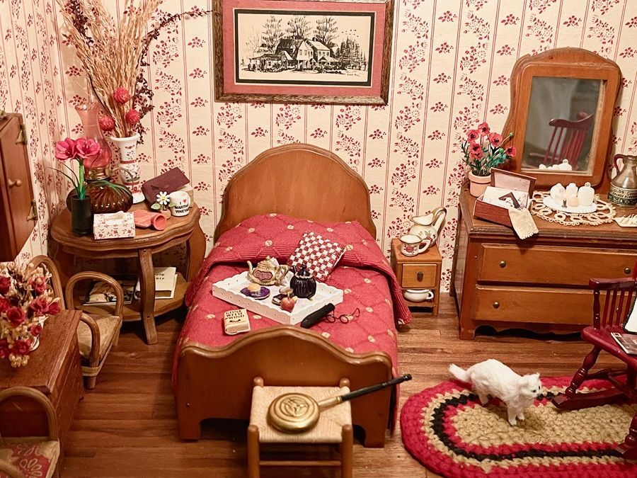 Cozy vintage bedroom with floral wallpaper, wooden bed, red bedding, and small furniture cluttered with decor