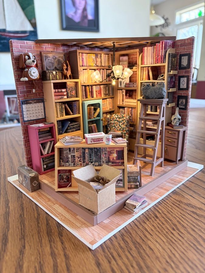 Detailed miniature bookstore diorama with shelves, ladders, books, and warm interior lighting on a wooden table