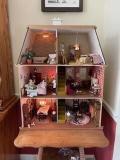 Three-story miniature dollhouse with warm-lit rooms and tiny furnishings on a wooden table.