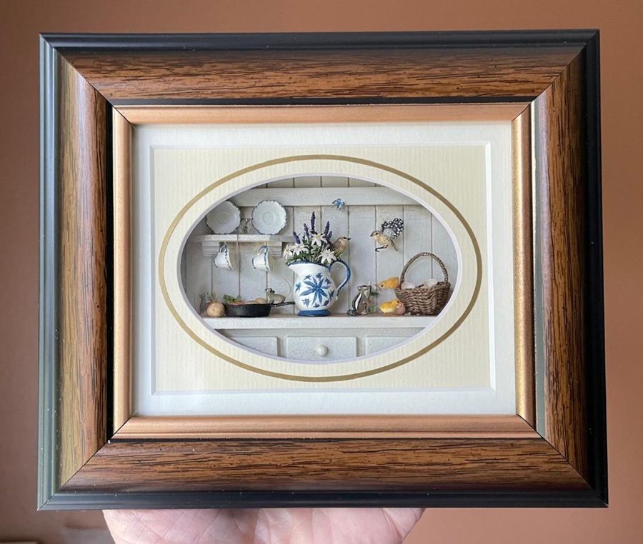 Wooden-framed oval shadowbox with a miniature tea set and porcelain dishes on display
