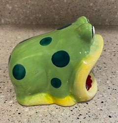 Green ceramic frog figurine with dark spots and an open red mouth on a speckled countertop
