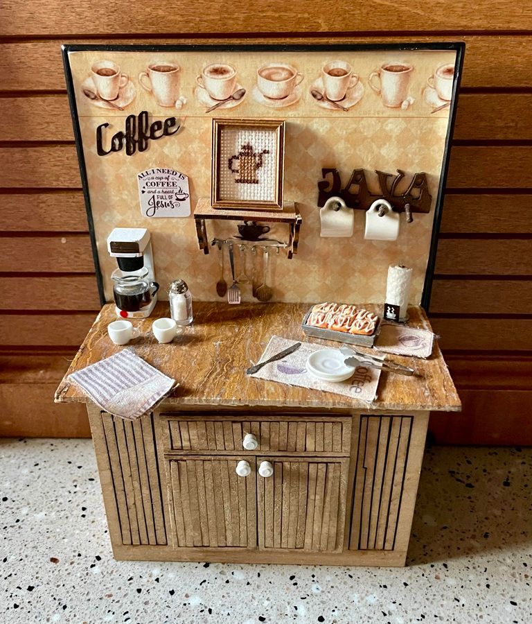 Miniature coffee bar with wood cabinets, cups, grinder, and countertop accessories against a wood wall.
