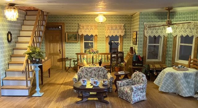 Cozy vintage living room with staircase, patterned wallpaper, armchairs, table, and warm lighting
