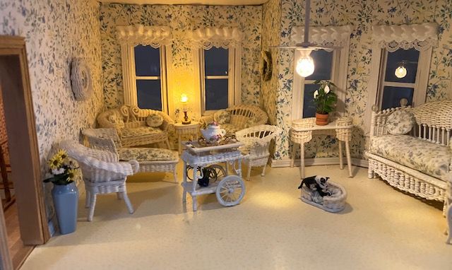 Cozy miniature living room with lace furniture, warm lights, patterned wallpaper, and a small dog on the floor