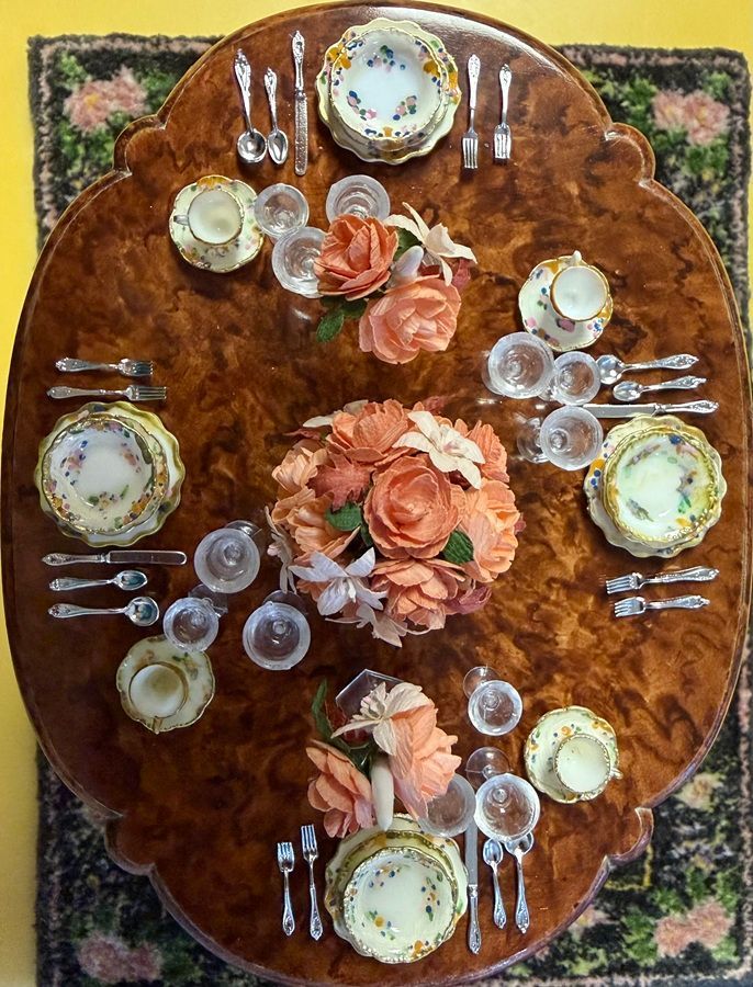 Overhead view of a floral table setting with plates, glasses, silverware, and peach roses on a brown cloth