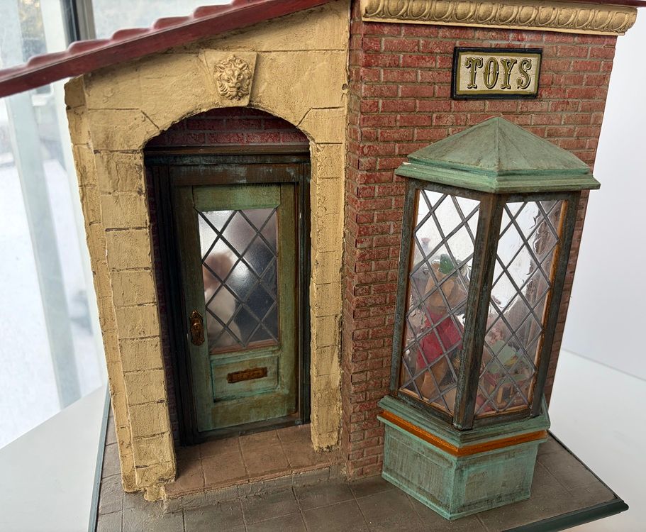 Miniature toy shop façade with a green door, brick walls, and a bay window display.