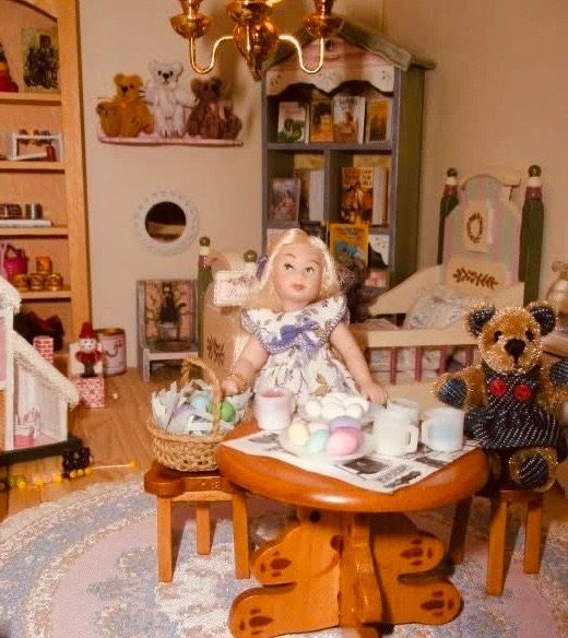 Doll seated at a tea table in a cozy miniature room, with a teddy bear and shelves of tiny decor nearby