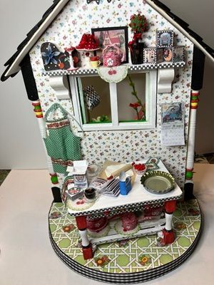 Miniature decorated dollhouse room with floral wallpaper, window, shelves, and tiny kitchen items on a circular base