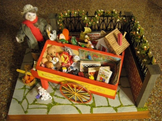 Miniature scene of a child with a red wagon full of toys beside a garden fence and gate